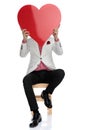 Seated modern man holding a big red heart over face Royalty Free Stock Photo