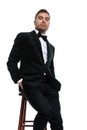 Seated unshaved businessman in black tuxedo holding hands in pockets Royalty Free Stock Photo