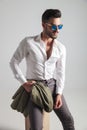 Seated young fashion man with sunglasses holding his jacket Royalty Free Stock Photo