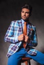 Seated young man in checkered suit holding his collar Royalty Free Stock Photo