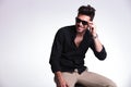 Seated young man holds his sunglasses and smiles Royalty Free Stock Photo