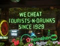 Bright green neon window sign photographed from street stating We Cheat Tourists-n-Drunks Since 1929