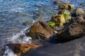 Seawater tide on mossy wet stones and black sand beach. Relaxing marine scene. Natural coast. Wet rocks on beach Royalty Free Stock Photo