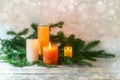 Second Advent, arrangement with four candles in orange and yellow, two are lit with a flame, fir branches on light rustic wood,