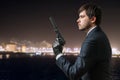 Secret agent holds pistol with silencer in hand at night