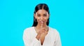 Secret, face and happy woman with finger on lips in studio, blue background or privacy sign. Portrait of indian model