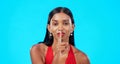 Secret, face and woman with finger on lips in studio, blue background and privacy sign. Portrait of indian model