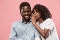 The young woman whispering a secret behind her hand to afro man Royalty Free Stock Photo