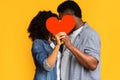 Secret Love. Romantic black couple hiding and kissing behind red paper heart Royalty Free Stock Photo