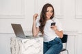 Secretary with a laptop and a phone in his hand. Young woman in white T-shirt and jeans looks at smartphone and smiles Royalty Free Stock Photo