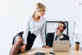 Secretary sitting on table while flirting with businessman