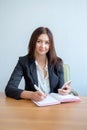 Secretary talking on mobile phone and writing notes while sitting at her desk. Royalty Free Stock Photo