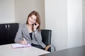 Secretary talking on mobile phone and writing notes while sitting at her desk. Royalty Free Stock Photo