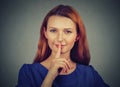 Secretive young woman placing finger on lips asking shh, quiet, silence