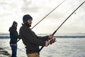 Secretly hoping hell hook the bigger fish...Shot of two young men fishing at the ocean in the early morning.