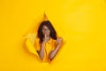Cheerful young woman poses in torn yellow paper hole background, emotional and expressive