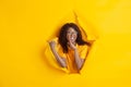 Cheerful young woman poses in torn yellow paper hole background, emotional and expressive