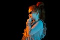 Secrets. Half-length portrait of cute redheaded little girl wearing festive dress isolated over dark background in neon