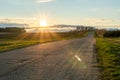 A section of paved road in a rural area passing by agricultural fields against the background of the setting sun and fluffy clouds Royalty Free Stock Photo