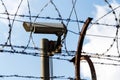 Security camera behind barbed wire fence on the wall, prison, security, crime or illegal immigration concept, blue sky Royalty Free Stock Photo