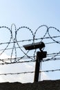 Security camera behind barbed wire fence on the wall, prison, security, crime or illegal immigration concept, blue sky Royalty Free Stock Photo