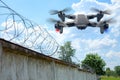 Security drone patrols the territory across the sky. Guarding the wall with barbed wire drone with blue and red beacon