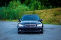 Sedan luxury black car parked in the parking lot near a forest-front view-hood, lights