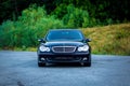 Sedan luxury black car parked in the parking lot near a forest-front view-hood, lights