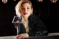 Seductive blonde in a green evening dress posing with a glass of red wine Royalty Free Stock Photo