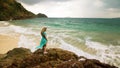 Woman walks on rock of sea reef stone, stormy cloudy ocean. Blue swimsuit dress tunic. Concept rest, tropical resort Royalty Free Stock Photo