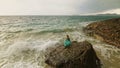 Woman walks on rock of sea reef stone, stormy cloudy ocean. Blue swimsuit dress tunic. Concept rest, tropical resort Royalty Free Stock Photo