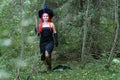 Seductive sorceress with red hair in a pointed hat in the forest is engaged in magic with a candle. Royalty Free Stock Photo