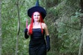 Seductive sorceress with red hair in a pointed hat in the forest is engaged in magic with a candle. Royalty Free Stock Photo