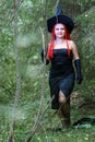 Seductive sorceress with red hair in a pointed hat in the forest is engaged in magic with a candle. Royalty Free Stock Photo