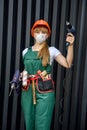 Seductive woman in coverall with drill machines in hands posing on abstract background with tool belt