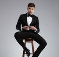 Seductive young man sitting and buttoning his black suit jacket Royalty Free Stock Photo