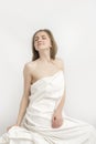 Seductive young woman dressed in sheet on white background. Portrait of naked caucasian girl, covered with sheet Royalty Free Stock Photo