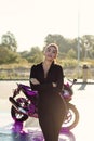 Seductive young woman in tight fitting black suit poses near sport motorcycle at self service car wash. Royalty Free Stock Photo