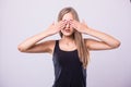 Portrait of young scared woman covering eyes with hands while standing against gray studio background. Confused girl close eyes wi Royalty Free Stock Photo