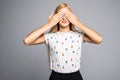 Portrait of young scared woman covering eyes with hands while standing against gray studio background. Confused girl close eyes wi Royalty Free Stock Photo