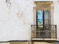 The view through the french window in a dreary weathered house facade in Portugal reveals the vibrant beauty of nature.