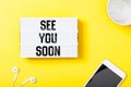 See you soon word in light box on office table flat lay