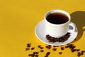 A cup of coffee with scattered coffee beans stands on a yellow background.