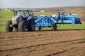 seeder drives along ploughed field against village forest