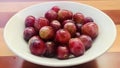 Seedless red grapes in white bowl, wooden table background. Royalty Free Stock Photo