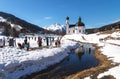 Cross-country skiers on sunny track along a river and a pitoresque church reflecting in the water, Seefeld, Austria