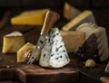 Segment of blue mould cheese and cheese knife on wooden board. Different cheeses at the background