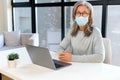 Seious mature gray-haired businesswoman wearing mask in modern office looks at the camera