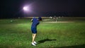 A man with a short pants holding a golf club playing at the golf driving range on a ground during the night Royalty Free Stock Photo