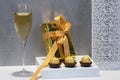 Select focus of a golden wrapped gift box with wrapped chocolate sweets and a glass of champagne